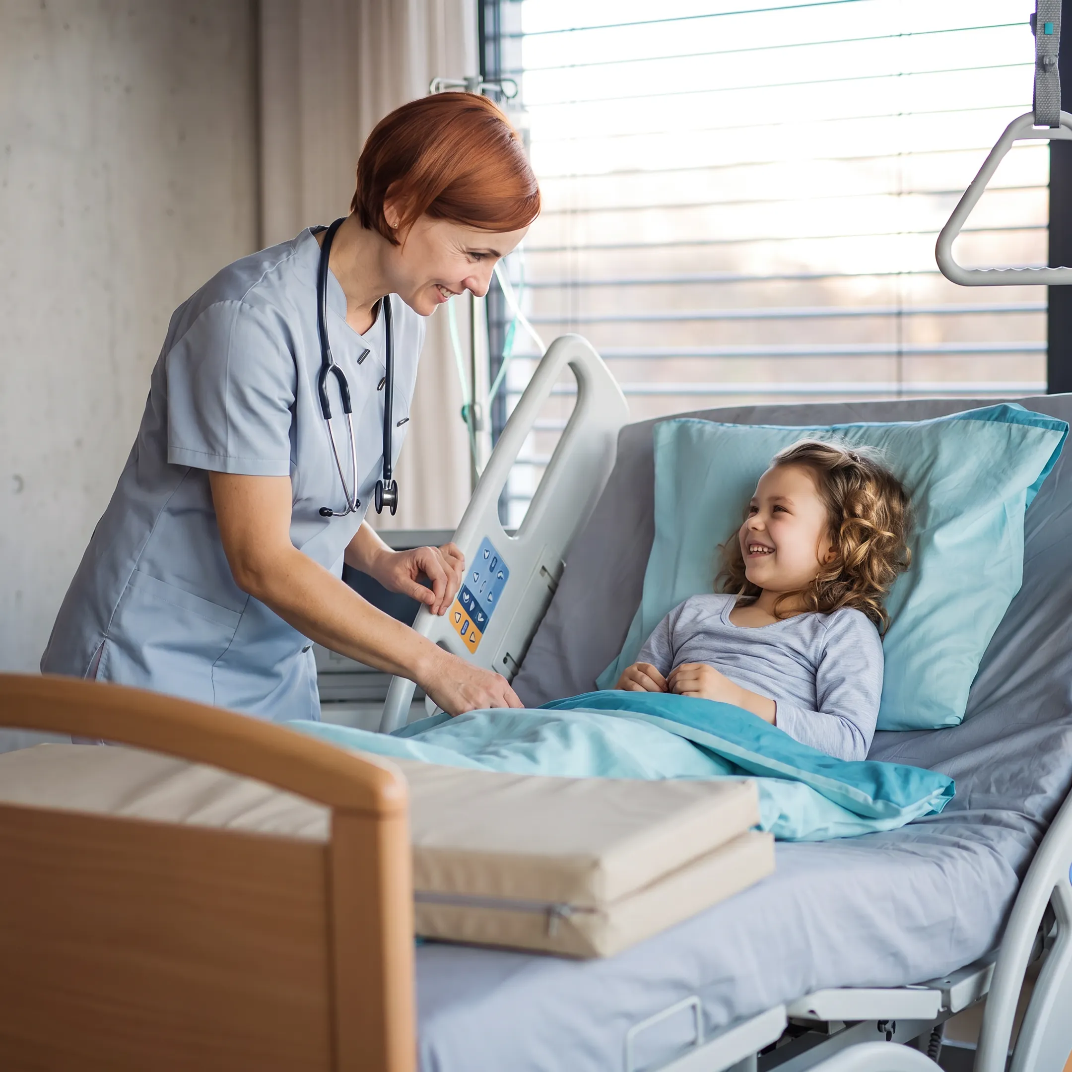 Caregiver adjusting a specialty hospital bed beside a therapeutic support surface