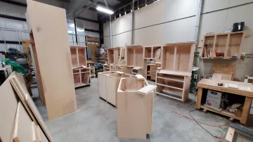 Artisan craftsman finishing a natural wood kitchen cabinet panel in a workshop