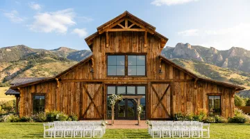 Historic rustic barn wedding venue with mountain panorama backdrop and outdoor lawn ceremony space