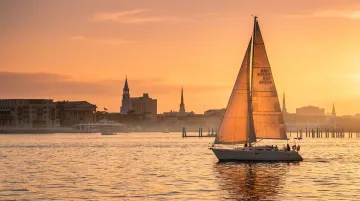 Historic Charleston harbor with sailboat at sunset and cobblestone waterfront