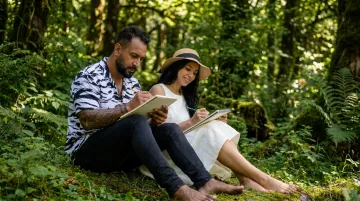 Couple sketching together outdoors in natural forest setting with sketchbooks