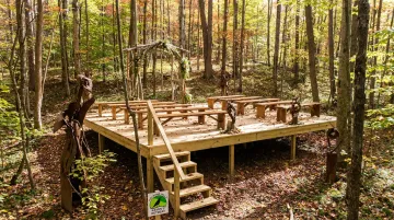 Raven's Retreat Hocking Hills forest ceremony platform surrounded by tall trees and sculptures