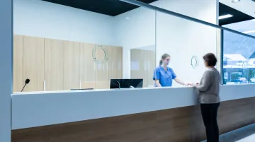 Hospital reception area with clear glass partition separating staff and patients