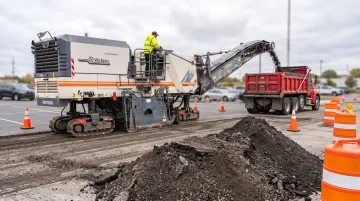 Highway milling machine cutting asphalt surface with traffic control setup
