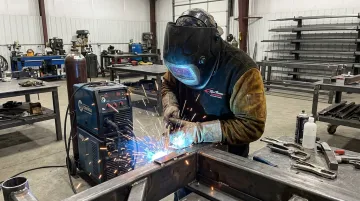 Certified welder operating TIG welding station on metal chassis component