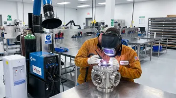 Certified TIG welder operating Miller TIG welding station on precision metal assembly