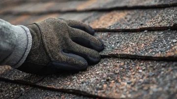 Roofing professional inspecting asphalt shingles on residential roof deck