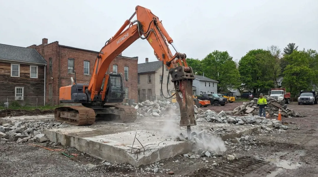 Excavator with breaker attachment performing concrete slab demolition on job site
