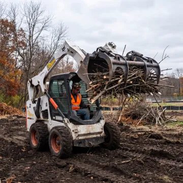 Operator moving brush with a grapple bucket