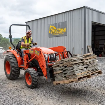 Tractor using bucket forks to move palletized materials