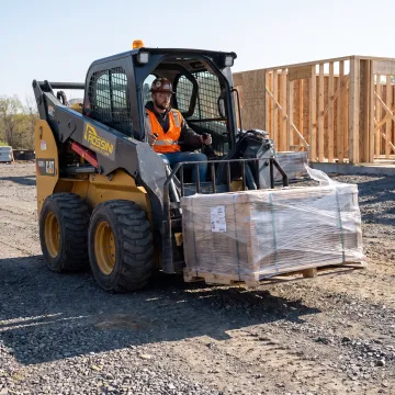 Operator using skid steer pallet forks at a job site