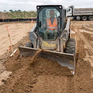 Operator grading soil with a skid steer dozer blade