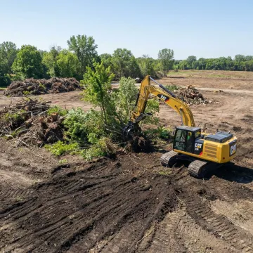 Heavy excavator clearing wooded land for construction site preparation