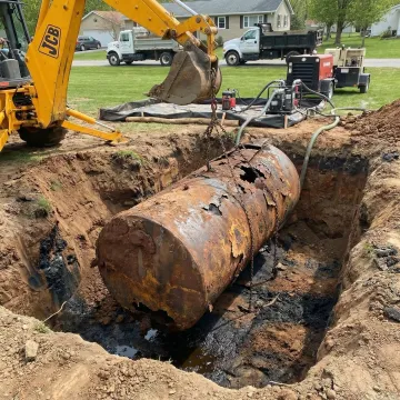 Excavator lifting extracted underground oil storage tank from excavation site