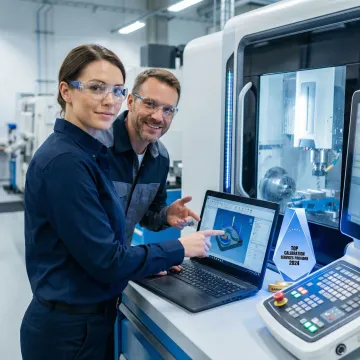Technician programming CNC machine while instructor reviews CAM software on laptop