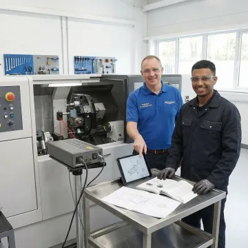 Manufacturing technician receiving hands-on CNC machine training in precision machining facility