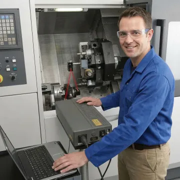 Technician using laser interferometer to calibrate CNC machine axes in manufacturing facility