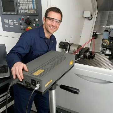 Technician performing linear axis calibration on CNC machine using laser interferometer