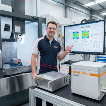 Calibration technician analyzing CNC machine measurement data on laptop in machine shop