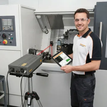 Precision laser interferometer measuring CNC machine axis alignment in manufacturing facility