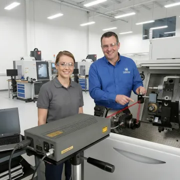 Instructor teaching CNC machinist student about precision measurement and machine calibration techniques