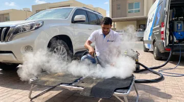 Mobile car detailing technician steam cleaning car floor mats