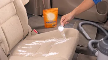 Person applying baking soda and vacuuming car seat upholstery
