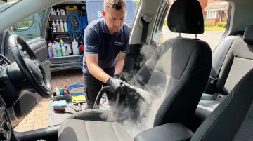 Mobile detailing technician steam cleaning car seat interior upholstery