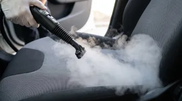 Handheld steam cleaner being used to clean car seat fabric upholstery