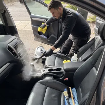 Technician steam-cleaning a vehicle interior