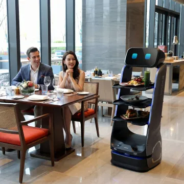 Food delivery robot serving guests at a restaurant table with trays of food