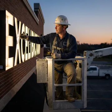 Technician in a bucket truck repairing an illuminated commercial sign.