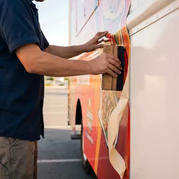 A technician carefully applying a custom vinyl wrap to the side of a food truck.