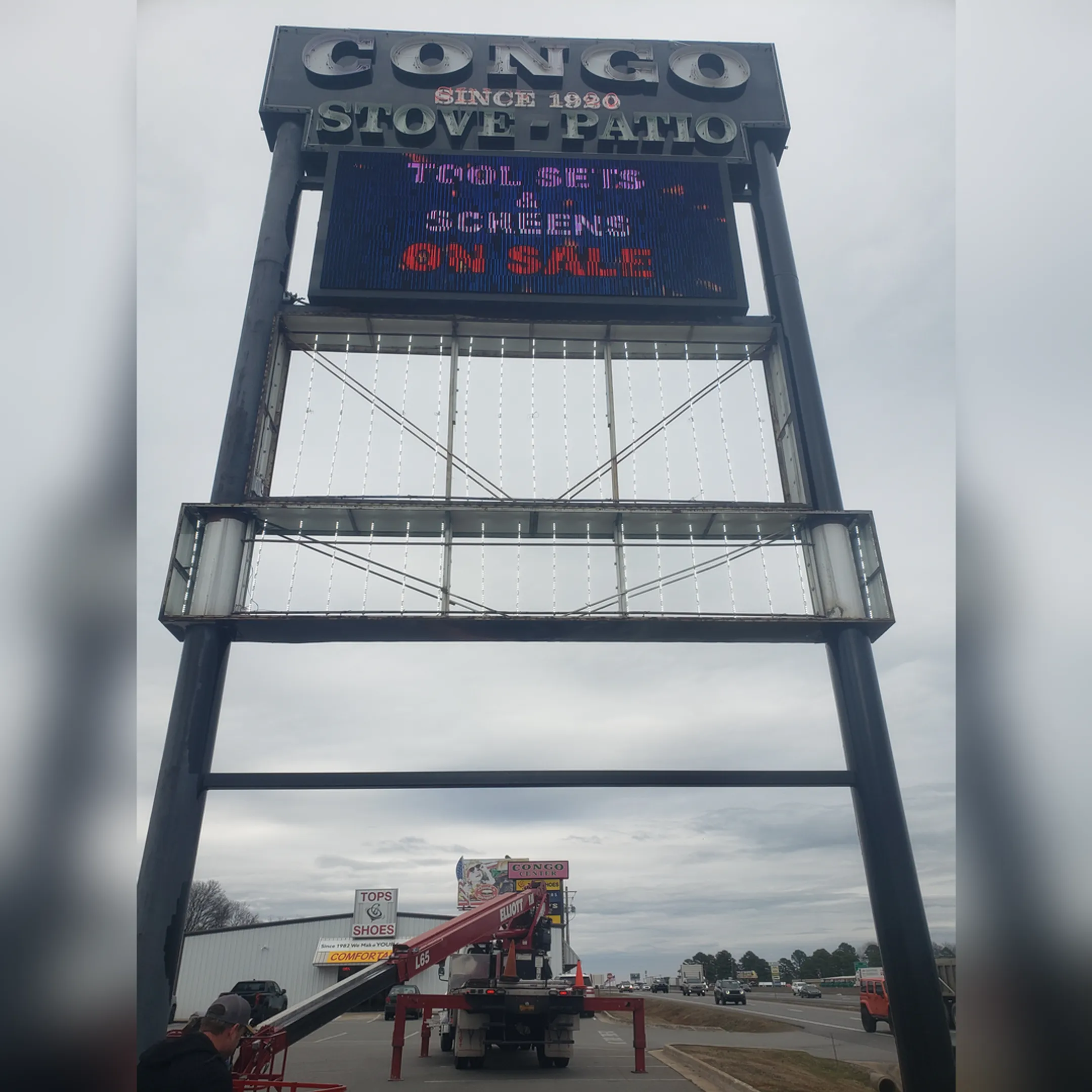 Technician in a bucket truck repairing an illuminated commercial sign.