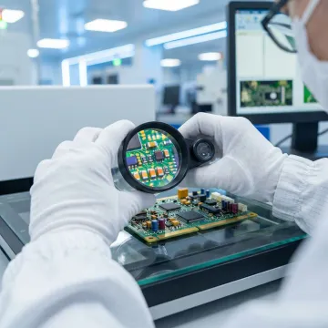 Technician inspecting assembled PCB under microscope in ISO-certified facility