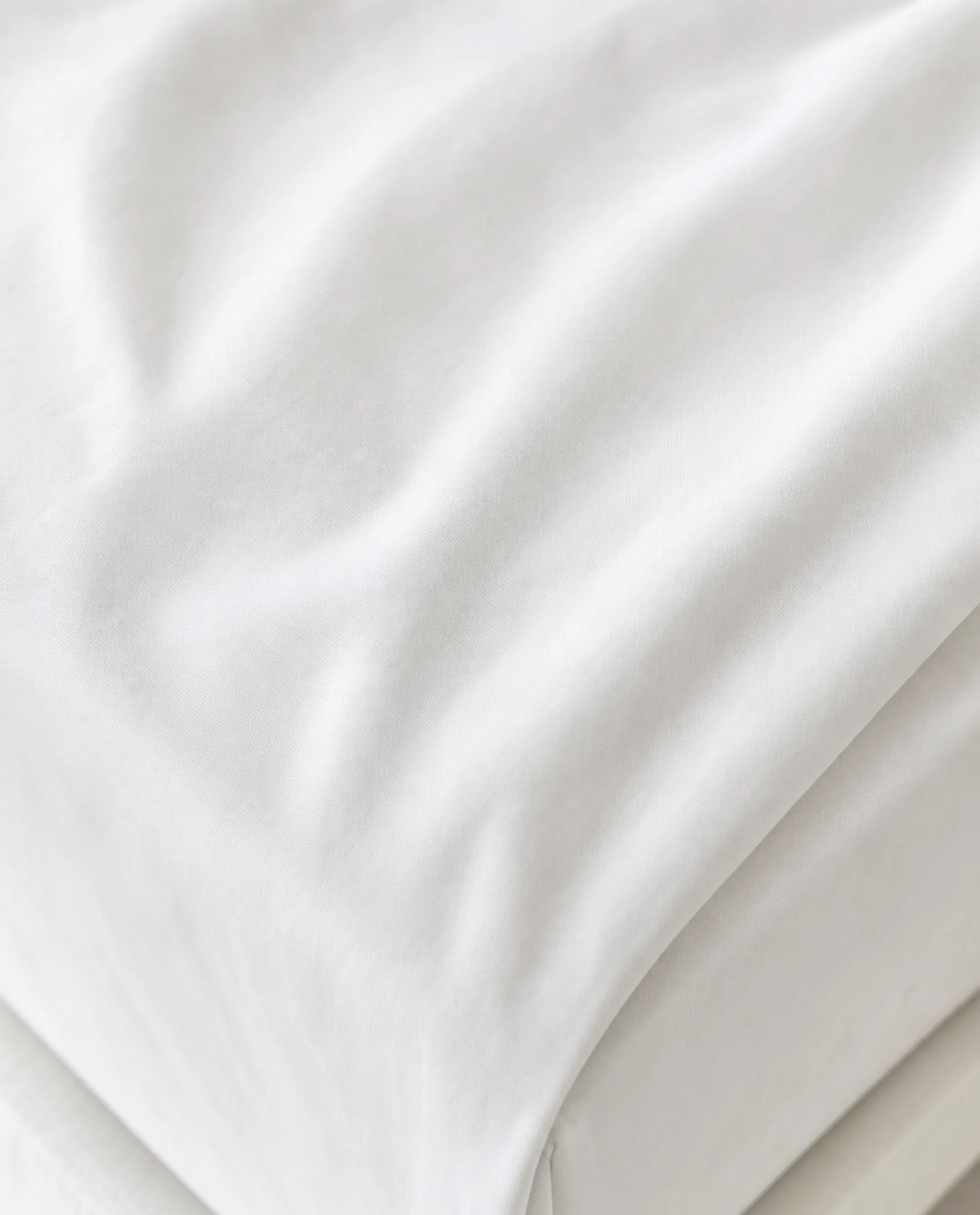 Close-up of crisp white percale cotton bed sheets on mattress