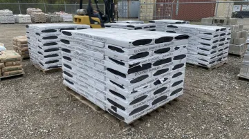 Bundled shingles and bagged aggregate stacked on wood pallets in warehouse