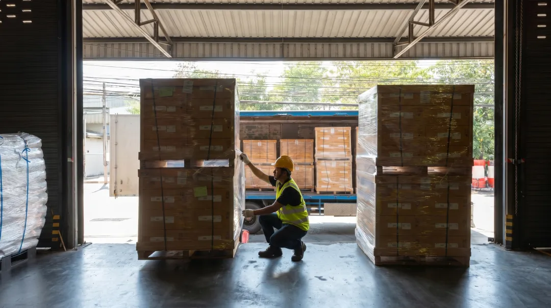 Warehouse worker inspecting wrapped pallet at loading dock before shipment
