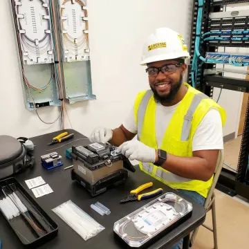 Technician performing fiber optic cable splicing and termination in network infrastructure deployment