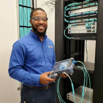 Network technician performing fiber optic cable termination and testing with certification equipment