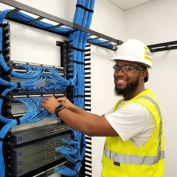 School IT technician installing network equipment in telecommunications closet with organized cable management