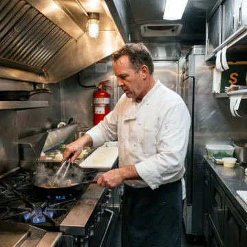 Chef preparing food inside a clean, modern food truck kitchen.