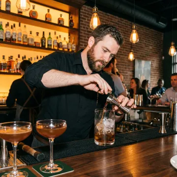 A bartender serving drinks in a lively Charlotte bar, with an overlay representing insurance protection.