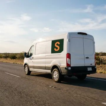A commercial van with a small business logo driving on a sunny Texas highway.