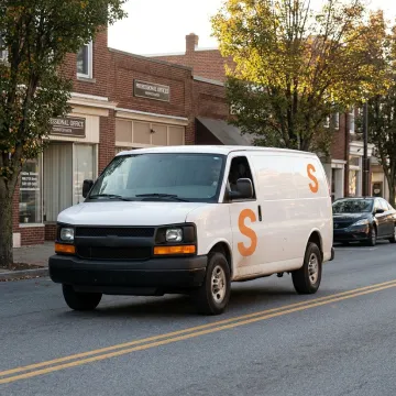 A commercial delivery van with a company logo driving through a business district in Somerset, Pennsylvania.
