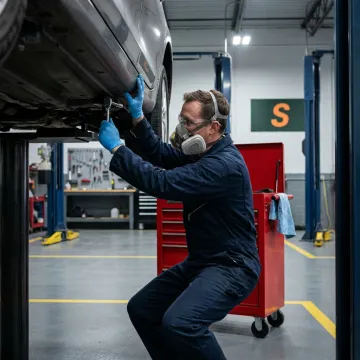 A certified auto body technician welding a car frame in a well-lit workshop.