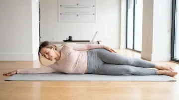 Postpartum woman performing side-lying Pilates exercise on mat with neutral spine