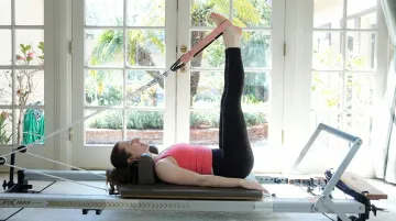Person performing hamstring stretch on Pilates Reformer using foot straps supine position