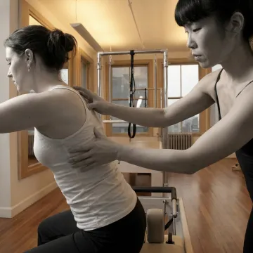 Instructor guiding a client on Pilates equipment