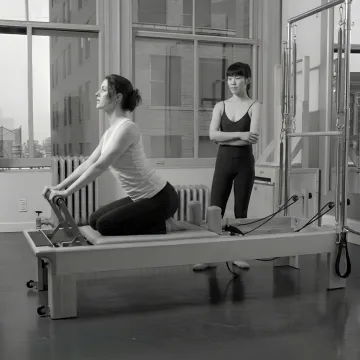 Instructor guiding intermediate reformer Pilates technique